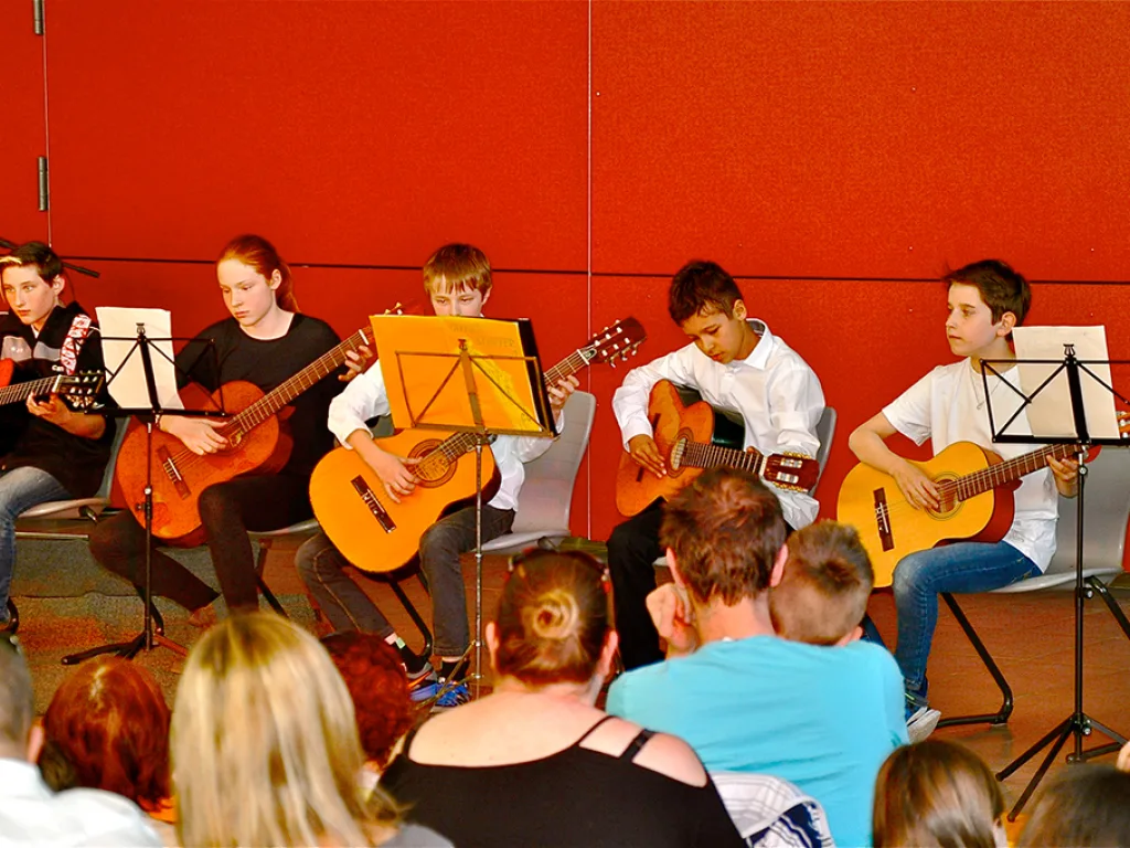 Eine Gitarrengruppe spielt an Notenständern vor Publikum.